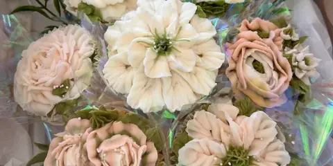A bouquet of cupcakes decorated with intricate white and pink buttercream flowers and green leaves.