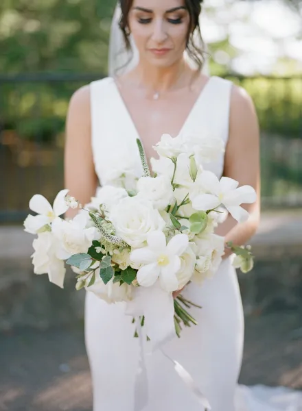 Bride in a white dress holding a bouquet of white roses and garden flowers