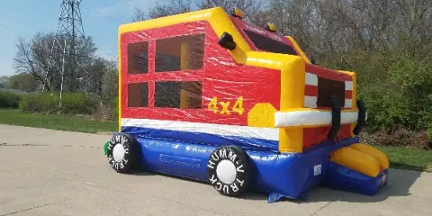 A colorful inflatable bouncer shaped like a truck, set up outdoors on a concrete surface.