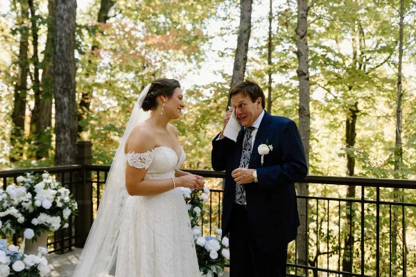 A bride in a white gown and a groom in a suit standing together at an outdoor wedding ceremony with floral arrangements.