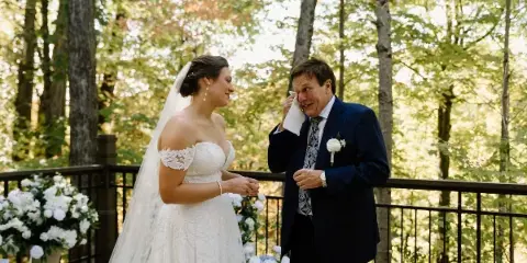A bride in a white gown and a groom in a suit standing together at an outdoor wedding ceremony with floral arrangements.