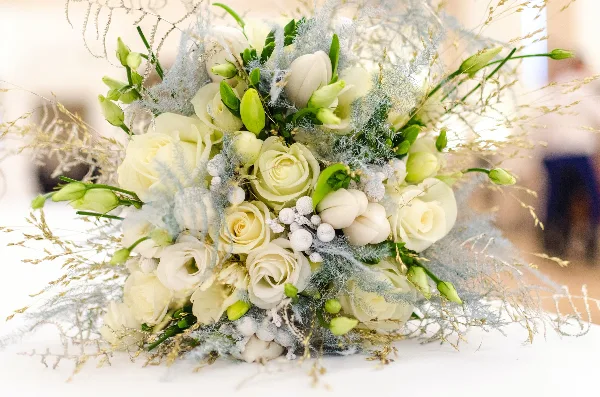 A close-up photograph of a white and green wedding floral arrangement featuring roses, calla lilies, and delicate greenery.