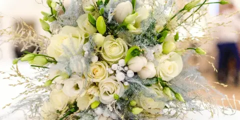 A close-up photograph of a white and green wedding floral arrangement featuring roses, calla lilies, and delicate greenery.