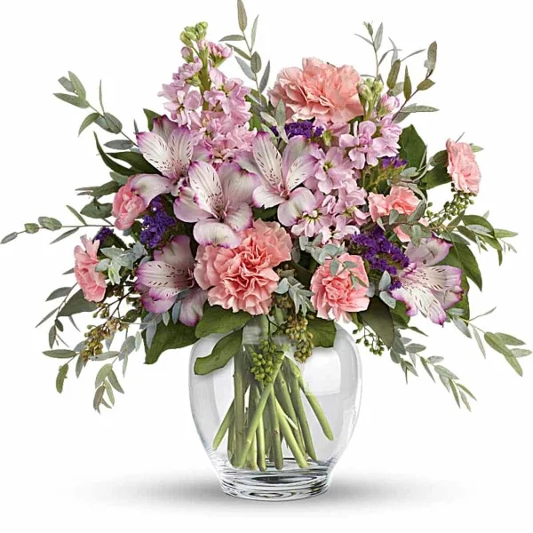 A mixed bouquet of pink and lavender flowers, including alstroemeria and carnations, arranged in a clear glass vase.