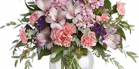 A mixed bouquet of pink and lavender flowers, including alstroemeria and carnations, arranged in a clear glass vase.