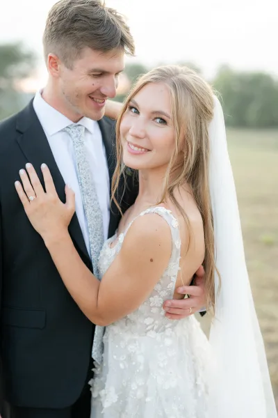 A bride and groom embracing, with the bride wearing a white wedding dress and veil and the groom in a suit.