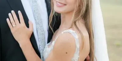A bride and groom embracing, with the bride wearing a white wedding dress and veil and the groom in a suit.