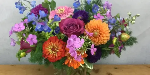 A colorful floral arrangement featuring roses, dahlias, and delphiniums in a glass vase.