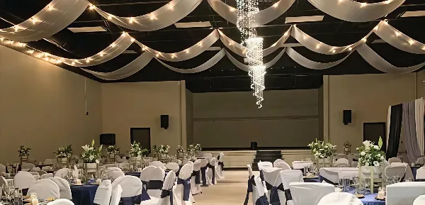 Interior view of a spacious event hall decorated with ceiling draping, a crystal chandelier, and round tables set for a wedding reception.