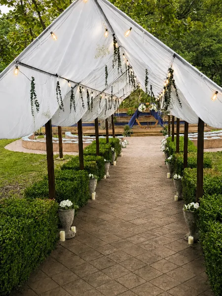 Decorated outdoor wedding aisle with a white canopy, string lights, and a ceremony arch.