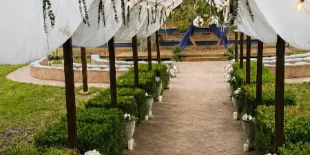 Decorated outdoor wedding aisle with a white canopy, string lights, and a ceremony arch.