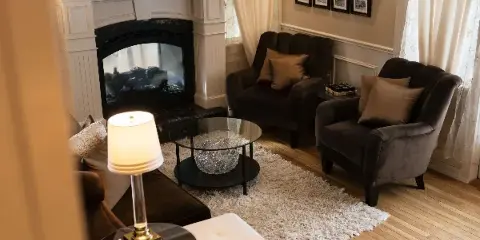 Interior view of a lounge featuring a white fireplace, dark armchairs, and a glass coffee table.