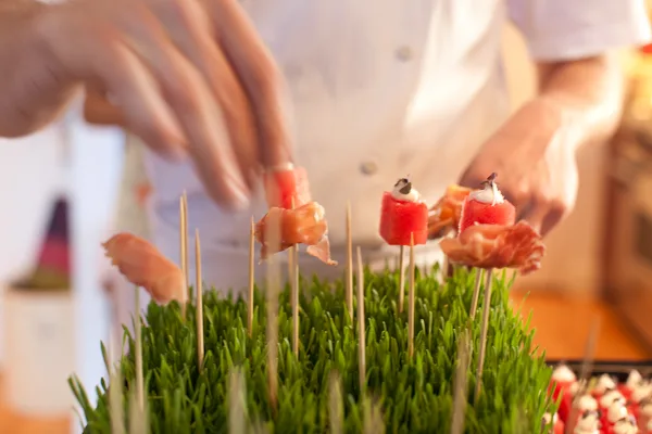 A chef's hands placing food skewers onto a bed of fresh green herbs.
