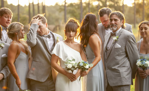 A wedding party, including the bride and groom, posing together outdoors during a photo session.