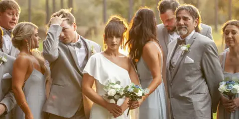 A wedding party, including the bride and groom, posing together outdoors during a photo session.