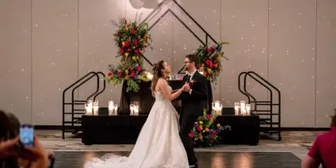 A bride and groom dancing at a wedding reception in front of a large floral arrangement and geometric metal structure.