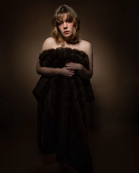 A fine-art studio portrait of a woman with wavy hair wearing a dark fur wrap against a dark background.