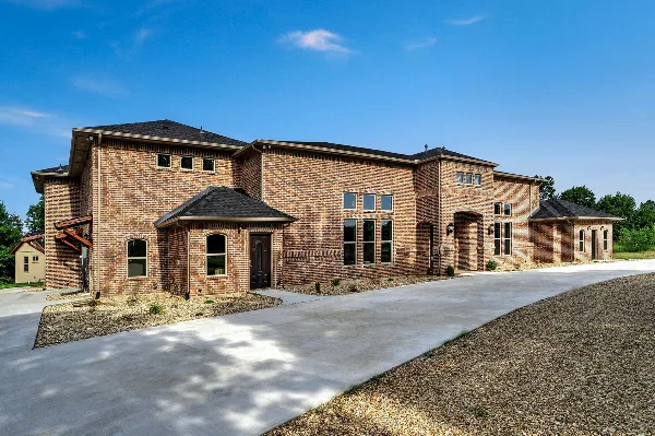 Exterior view of a large brick event venue building with a paved driveway and gravel landscaping under a blue sky.