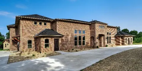 Exterior view of a large brick event venue building with a paved driveway and gravel landscaping under a blue sky.