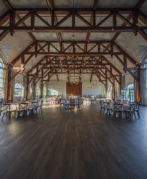 Interior of a large banquet hall with exposed wooden beams, chandeliers, and round tables set for a formal event.