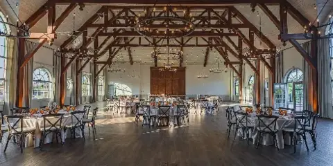 Interior of a large banquet hall with exposed wooden beams, chandeliers, and round tables set for a formal event.