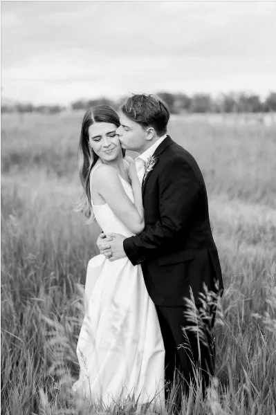 A black and white photograph of a bride and groom embracing in a grassy field.