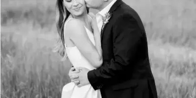 A black and white photograph of a bride and groom embracing in a grassy field.