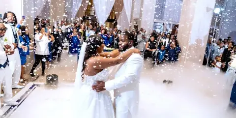 A bride and groom dancing in a grand historic venue with marble floors and high ceilings, surrounded by guests and falling confetti.