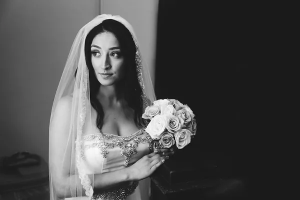 A black-and-white photograph of a bride wearing a veil and holding a bouquet of roses.