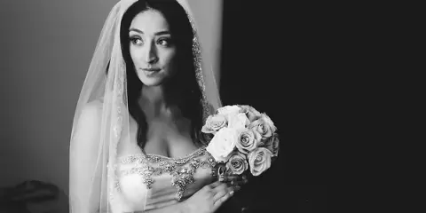 A black-and-white photograph of a bride wearing a veil and holding a bouquet of roses.