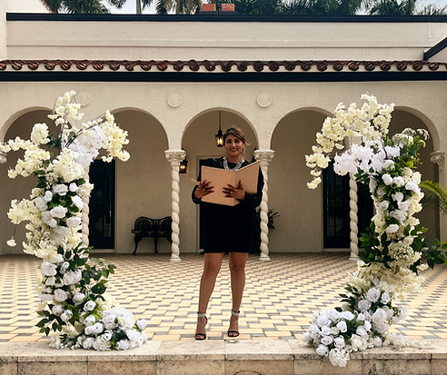 A wedding officiant standing at a floral-decorated altar during an outdoor ceremony at a luxury estate venue.