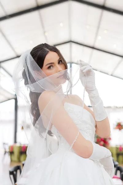 A bride in a white wedding dress and veil looking over her shoulder with styled hair and makeup.