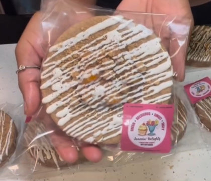 A hand holding a packaged gourmet cookie with white icing drizzle and a Jonesin' Delightz logo sticker.