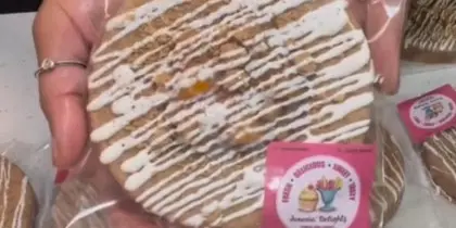 A hand holding a packaged gourmet cookie with white icing drizzle and a Jonesin' Delightz logo sticker.