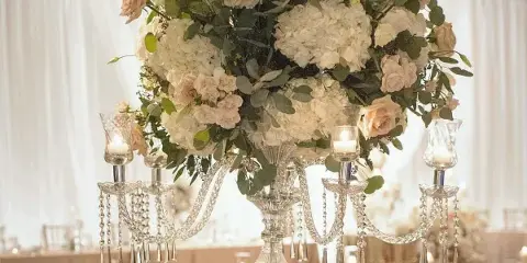 Elegant floral centerpiece with white hydrangeas and pink roses on a crystal candelabra stand in a banquet hall.