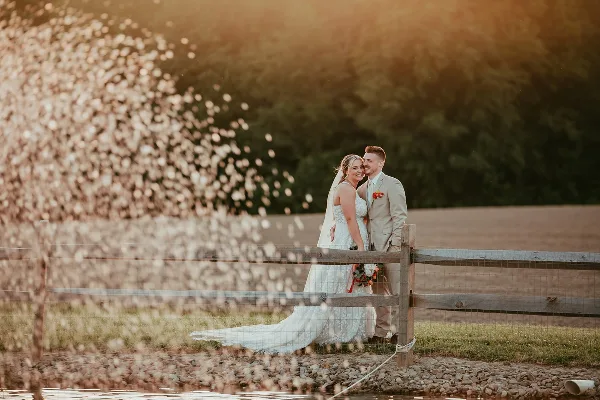A bride and groom standing together by a wooden fence with confetti falling in the foreground.