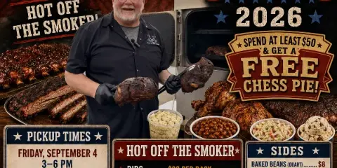 A man in a black shirt holding two pieces of smoked meat in front of a smoker and a table of catering food.