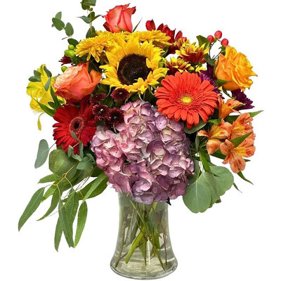A colorful floral arrangement featuring sunflowers, roses, and hydrangeas in a glass vase.