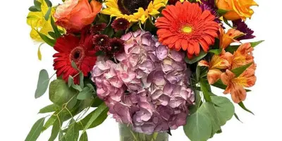 A colorful floral arrangement featuring sunflowers, roses, and hydrangeas in a glass vase.
