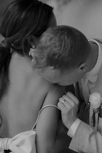 Black and white photograph of a groom kissing the shoulder of a bride wearing a wedding dress and earrings.