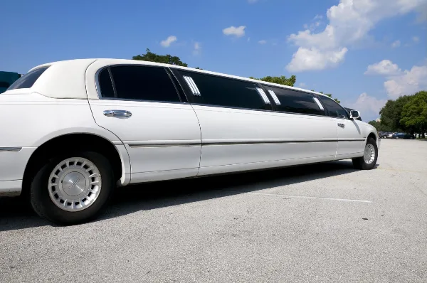 A white stretch limousine parked in a lot under a blue sky.