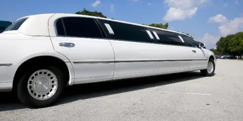 A white stretch limousine parked in a lot under a blue sky.