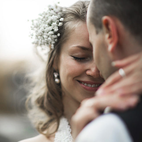 A close-up photograph of a smiling bride with a floral headpiece and a groom in an intimate embrace.