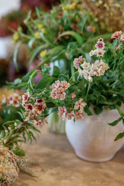 A close-up of a floral arrangement with garden roses and greenery in a white ceramic vase.
