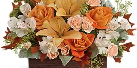 A floral arrangement featuring orange roses, yellow lilies, and white alstroemeria in a rectangular wooden box.