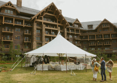A large white event tent set up on a grassy lawn in front of a large lodge-style building, with tables and chairs visible inside.