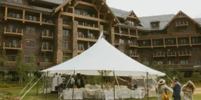 A large white event tent set up on a grassy lawn in front of a large lodge-style building, with tables and chairs visible inside.