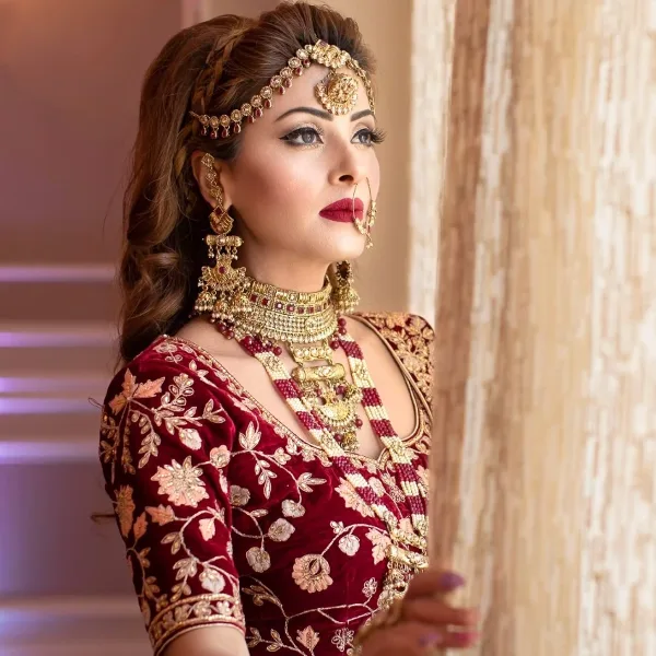 Bride in red embroidered outfit with styled hair, gold jewelry, and full makeup