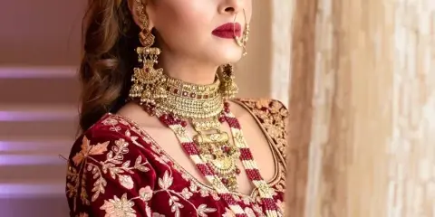 Bride in red embroidered outfit with styled hair, gold jewelry, and full makeup