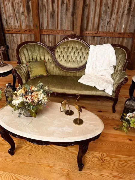 A vintage green tufted sofa and marble coffee table styled with floral arrangements and decorative items in a rustic setting.